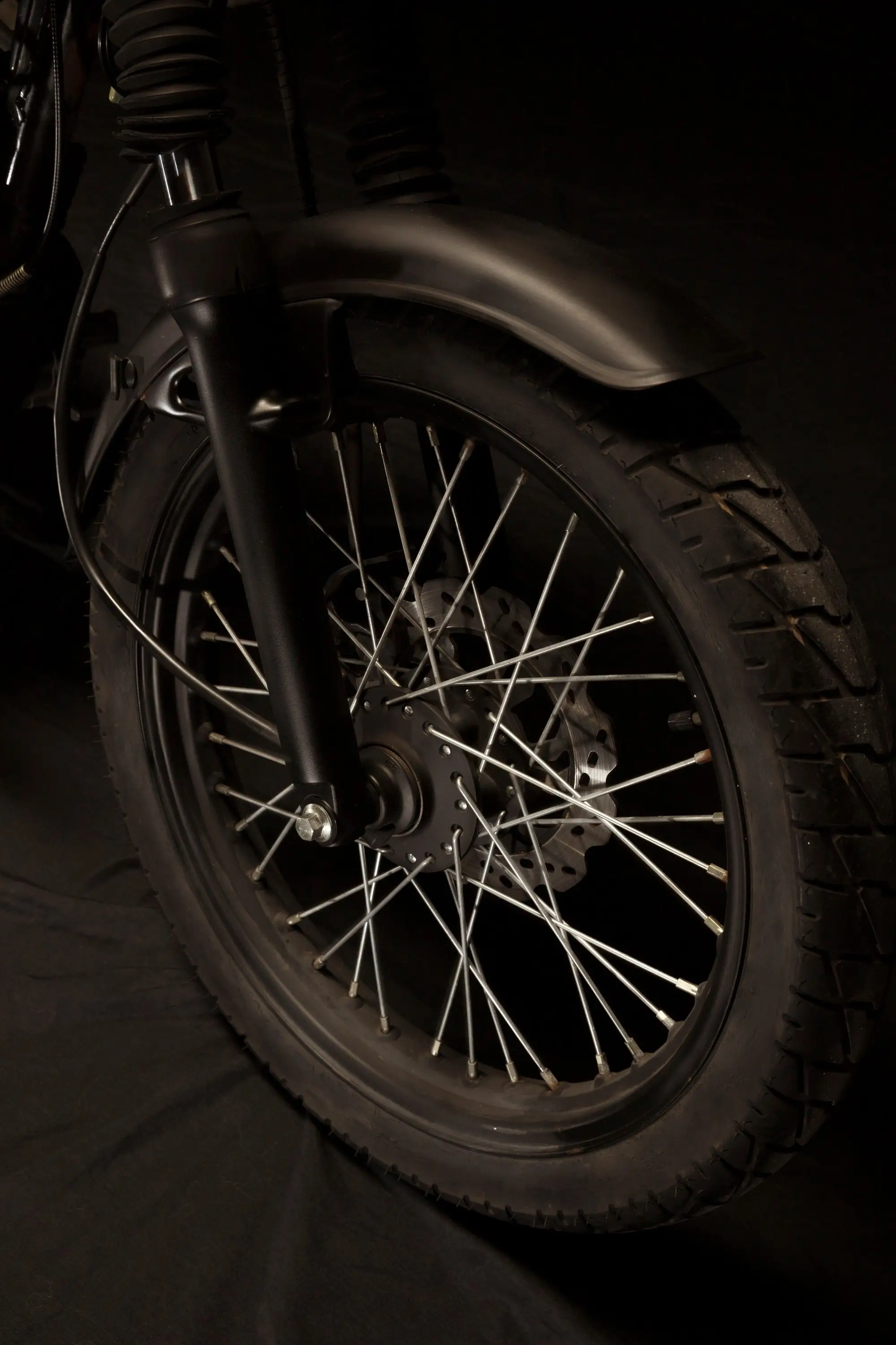 Close da roda dianteira de uma moto, raios cromados e disco de freio