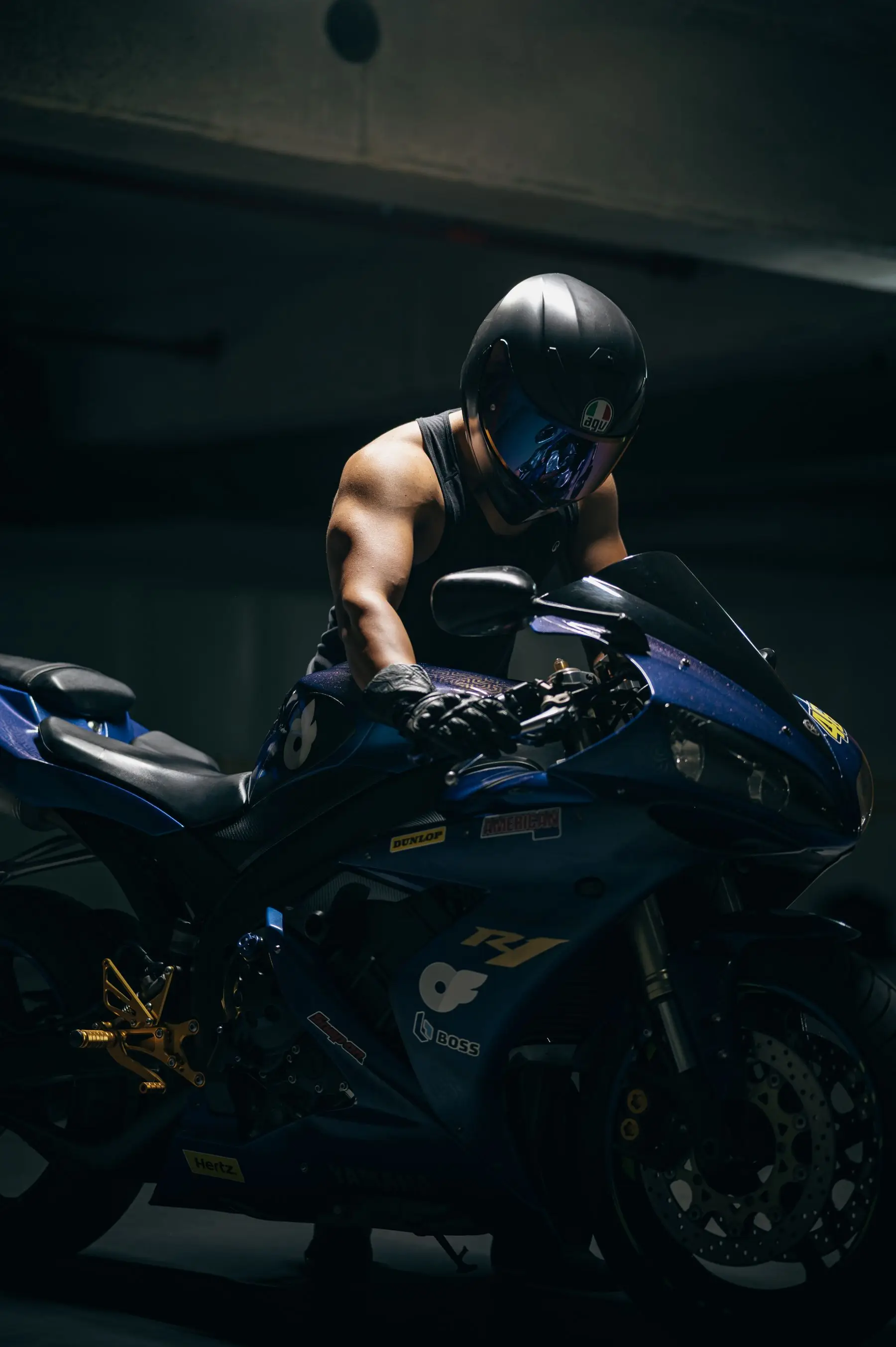 Motociclista de capacete apoiado na sua esportiva, numa garagem escura